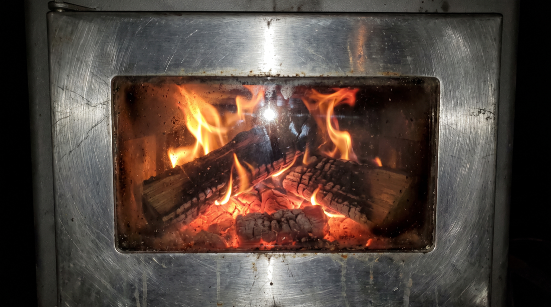 Wood fire burning on a bed of coals seen through the glass window of a tent stove door