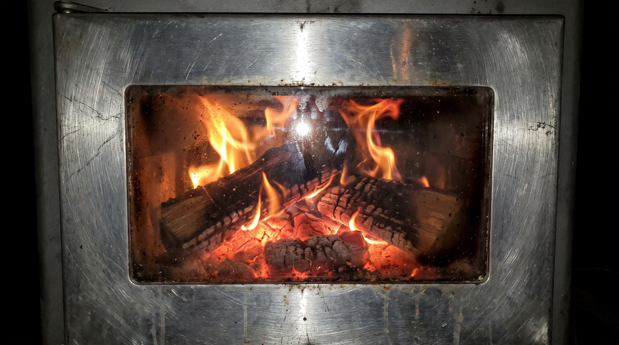 Wood fire burning on a bed of coals seen through the glass window of a tent stove door